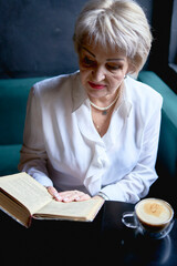  an elderly woman reads a book in a cafe and drink coffee
