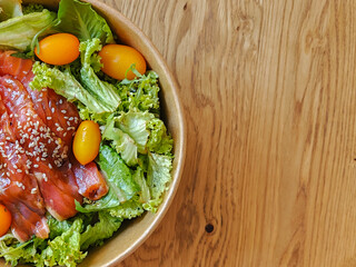 Healthy poke bowl dish with salmon and vegetables in kraft paper packaging on a wooden table. Takeout food. Close-up