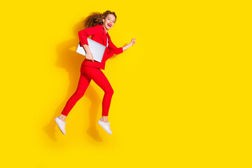 Full size photo of pretty young woman netbook jump empty space wear red suit isolated on yellow color background
