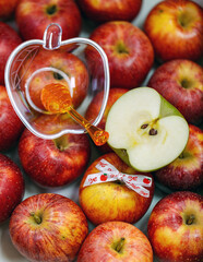 Clear apple shaped plastic container with a honey dipper inside, ribbon with the text Shana Tova in Hebrew which means Good Year in English and one apple cut in half it rests on top of the red apples
