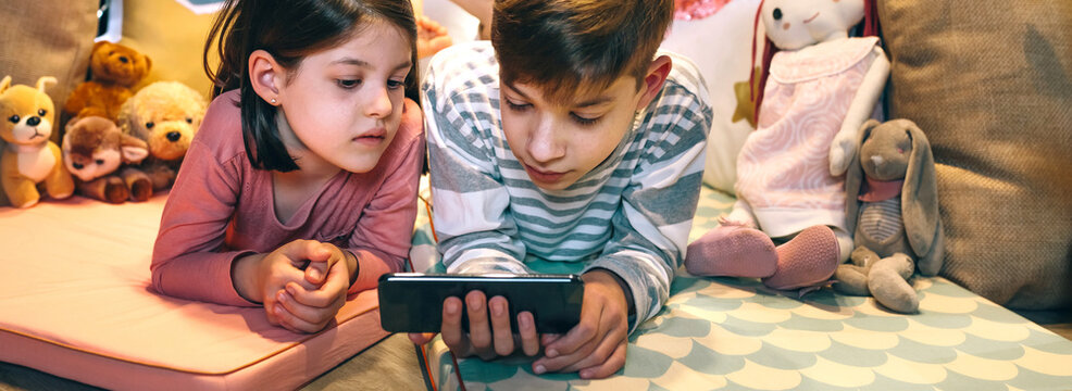 Banner of children watching unsafe content on cellphone without parental supervision. Girl and boy lying together while chatting with strangers on social network app. Screen addiction dangers concept.