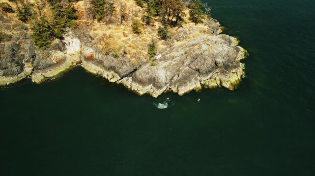Drone shot capturing friends jumping off a small cliff side at the edge of an island into the tropical blue green water on a sunny summer day