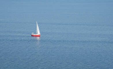 Fototapeta premium White sailboat sailing on calm blue sea from island clifftop