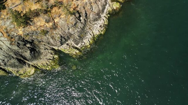 Top down drone shot of the waters edge of a small tropical island with clear blue ocean water crashing on the coastline rocks calmly as the drone lowers