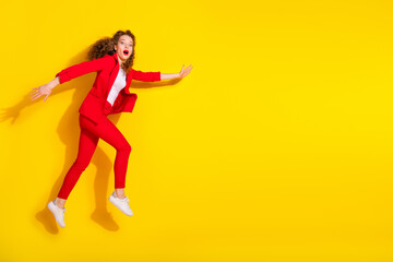 Full size photo of pretty young woman jump rush empty space wear red suit isolated on yellow color background