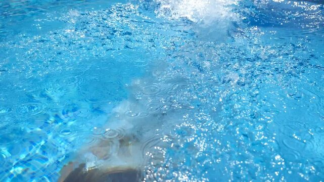 Unrecognizable woman jumping in pool and splashing crystal clear water. Young girl in swimsuit swimming under water in basin of hotel. Lady relaxing during summer vacation. Slow motion Close up