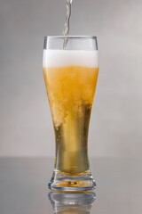 Beer. Glass of fresh and cold beer. Pouring craft beer on a gray background with reflection. Stream of draught beer in glass. Glass of fresh and cold light beer.  Shallow depth of field