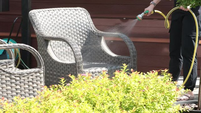 Anonymous cleaning, hose water washing wicker furniture from summer. Structures in backyard. Cleanliness and order. 