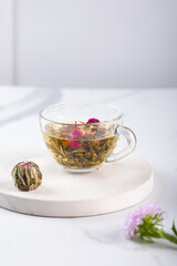 Tea ceremony. Glass teapot with blooming tea flowers served at elegant marble grey background.