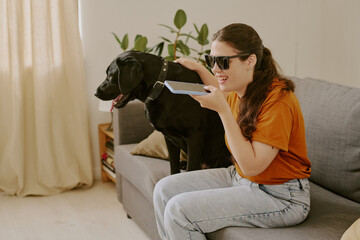 Happy woman with disability petting her black Labrador while speaking on smartphone