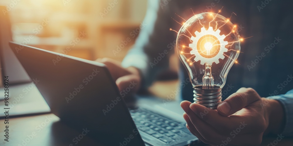 Aufkleber A man holds a light bulb with a gear icon inside while using a notebook computer, representing the inspiration for innovative ideas through online technology.