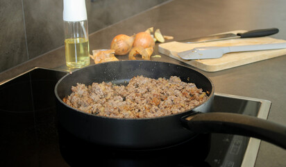 Close up cooked ground beef meat frying in a pan in the kitchen, blurry background with onions and oil spray 