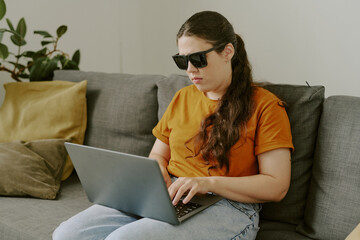 Blind woman sitting on couch and typing on keyboard while resting