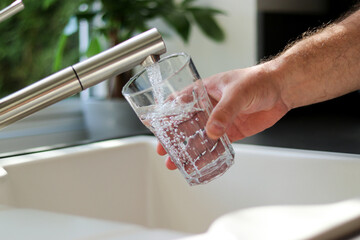 Close up of male hands pouring tap water into a glass in the kitchen