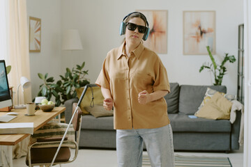Brunette woman with disability wearing turquoise headphones and listening to music while dancing alone