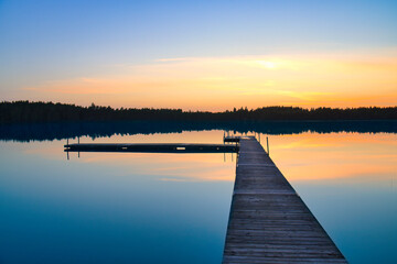 Naklejka premium Wooden jetty at sunset on a Swedish lake. The colors are reflected in the water