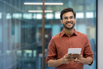 Smiling businessman holding tablet in office setting conveys confidence and engagement with...