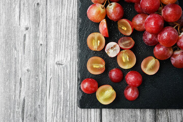 A bunch of large pink grapes next to cut grapes on a black tray on a gray wooden background