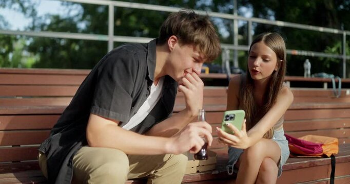 A happy guy in a black shirt looks at the TV that his girlfriend a classmate is showing him during a conversation and a picnic in the park