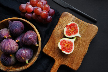 Ripe whole and sliced ​​figs next to pink grapes on a wooden board on a dark background