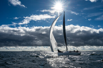 Segelyacht mit Gennaker vor atemberaubenden Wolken mit Sonne 