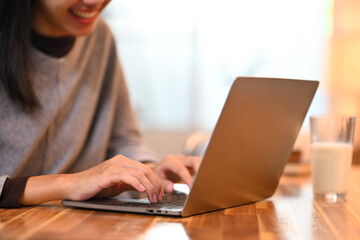 Fototapeta premium Smiling young woman sitting at kitchen counter with a glass of milk and working with laptop