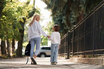 Fototapeta premium Rear view, walking. Schoolgirl with her mother are outdoors together
