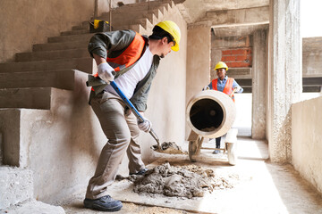 Multiethnic male and female masons mixing cement near mixer in corridor at construction site