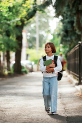Fototapeta premium Holding notepad. Schoolgirl with backpack is outdoors