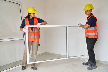 Full length of carpenters wearing safety workwear installing window frame in house construction site