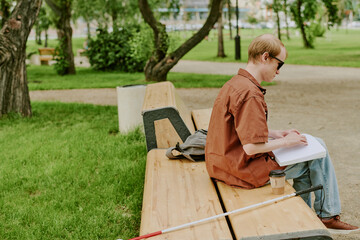 Unrecognizable man sitting on wooden bench and enjoying Braille book in park
