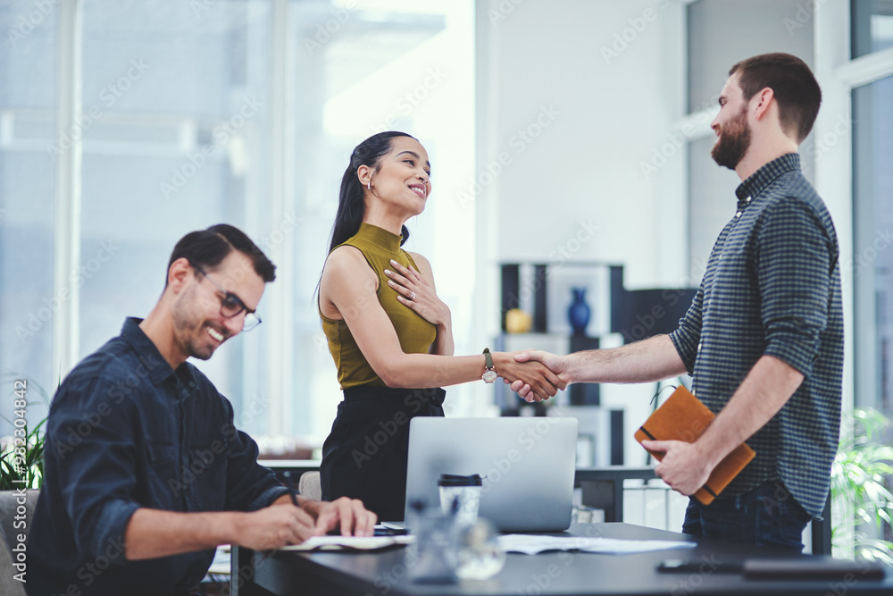 Wall mural Handshake, thank you and smile in office, people and meeting for project, paperwork or celebration. Colleagues, holding hands and creative for journalism, laptop and proud of collaboration or article