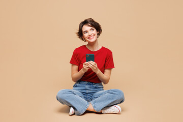 Full body young smiling happy woman she wears red t-shirt casual clothes sits hold in hand use...