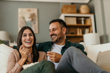 An adult couple watch movie, series on television and eat popcorn at home