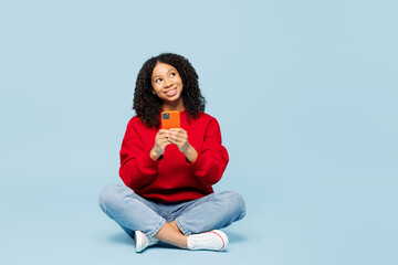 Full body little kid teen girl of African American ethnicity wear red sweatshirt sits talk speak on...