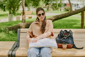 Young brunette woman with disability wearing sunglasses and reading Braille novel while enjoying...