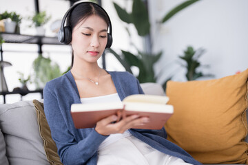 Concentrated Young asian woman Student Research With book and Headphones on sofa at home Studying Online concept