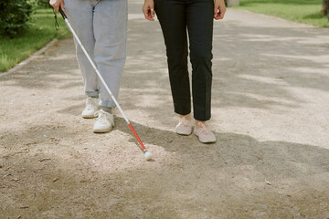 Unrecognizable friends walking in park, person with disability using meta cane to orientate while walking