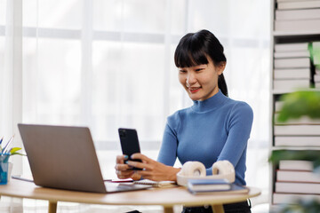 Smile asian woman working from home on laptop, freelance work online with phone and laptop documents 