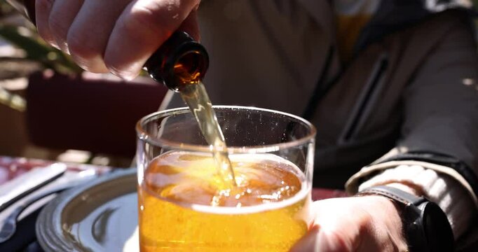 Male hands pour draft beer from bottle into glass. Fresh light foamy beer with gas bubbles