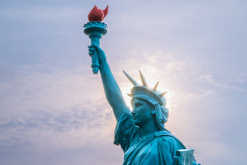 Fototapeta premium A replica of the Statue of Liberty stands as a beacon of hope against a setting sun. The statue's torch casts a warm glow, illuminating the surrounding area. Shimen, New Taipei City, Taiwan.