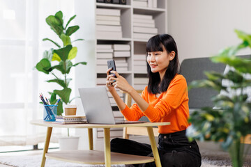 business woman talking with somebody while sitting at home and working on laptop. Happy business woman chatting on digital gadgets online, holding mobile phone, using laptop
