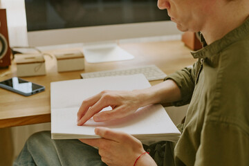 Side view shot of unrecognizable man with disability focused on Braille book