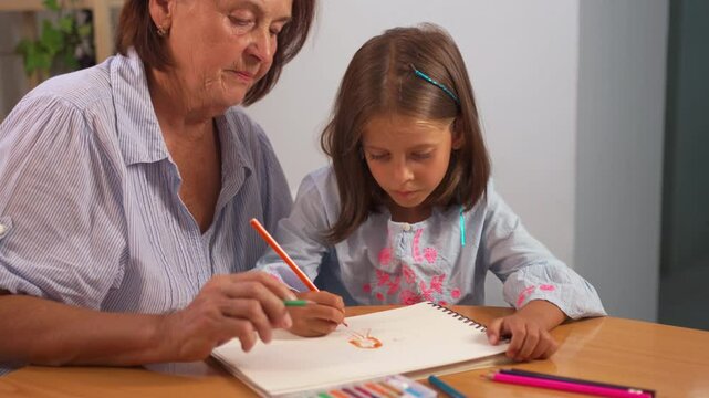 Focused grandmother and granddaughter coloring in book together on table at home. The scene is filled with creativity and warmth, as they bond over their artistic activity - Powered by Adobe