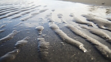 A close-up of wet sand with water receding, leaving reflective patterns along the beach.
