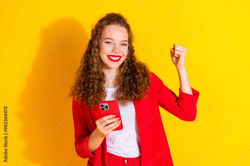 Wall mural Photo of pretty young woman smart phone raise fist wear red suit isolated on yellow color background