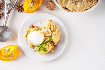 Homemade autumn pumpkin crisp cobbler, pumpkin crumble pie with crunchy dough topping in baking dish and plate, with ice cream scoop on white kitchen table