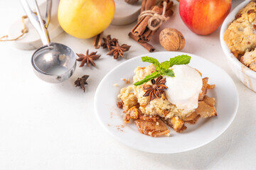 Apple Crumble Dessert, crisp cobbler with Ice Cream, crumble pie with crunchy dough topping in baking dish and plate, with ice cream scoop on white kitchen table