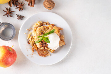Apple Crumble Dessert, crisp cobbler with Ice Cream, crumble pie with crunchy dough topping in baking dish and plate, with ice cream scoop on white kitchen table