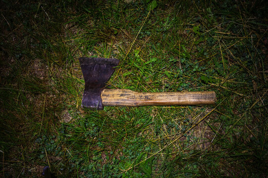 An axe lies on the grass at night. An old axe is thrown on the ground